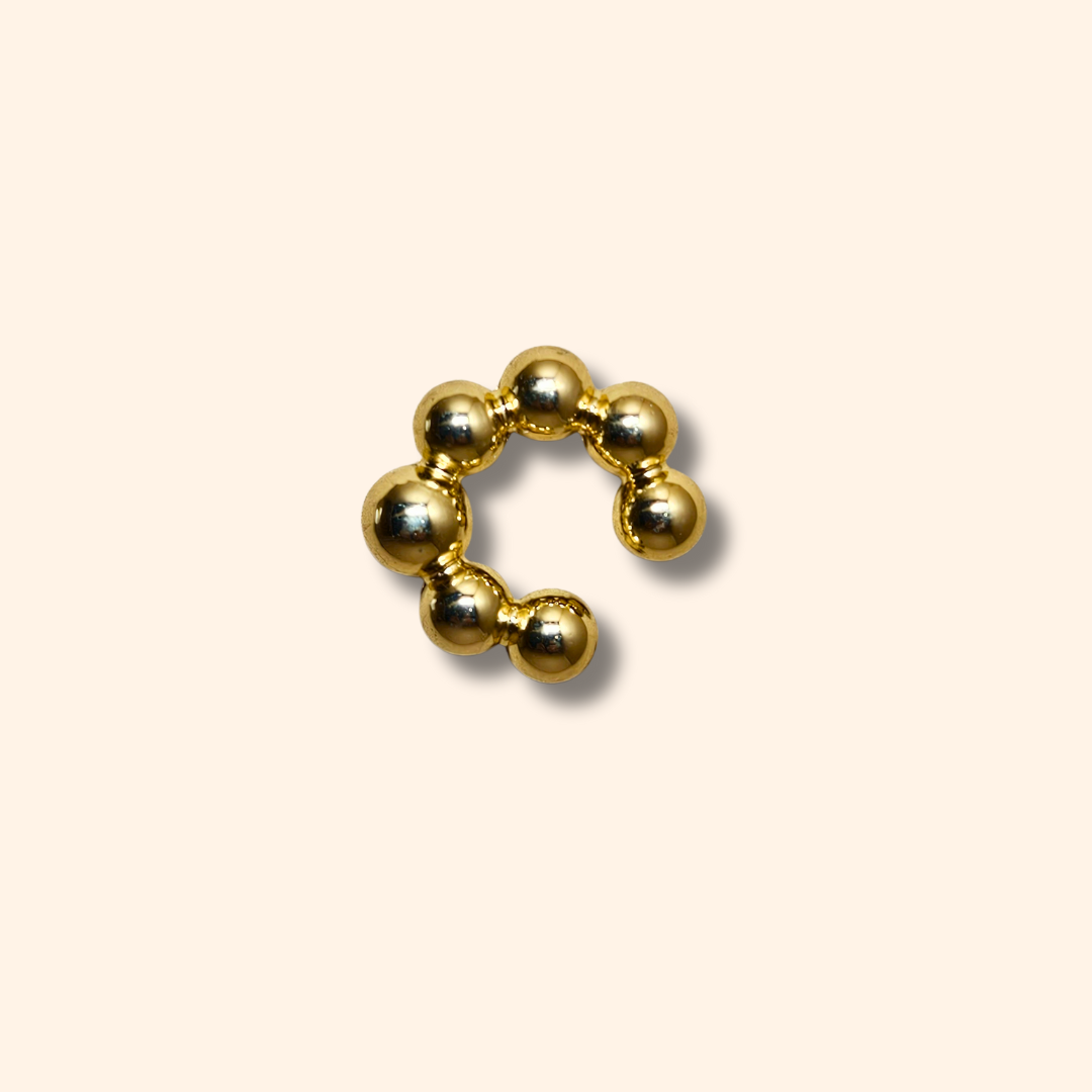 The Seven Spheres Ear Cuff by Roots Jewellery, crafted from stainless steel, is a fashionable accessory adorned with gold beads elegantly set against a beige background.