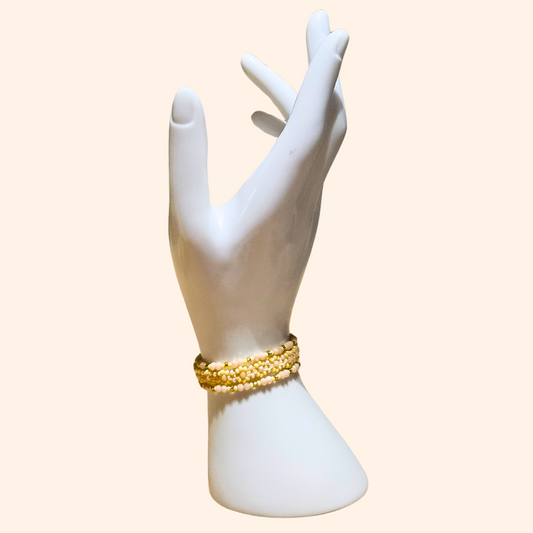 The mannequin elegantly showcases the Golden Dawn Beaded 3-Set Bracelet from Roots Jewellery, with its gold accents and pearls shimmering in harmony with subtle pastel yellows.