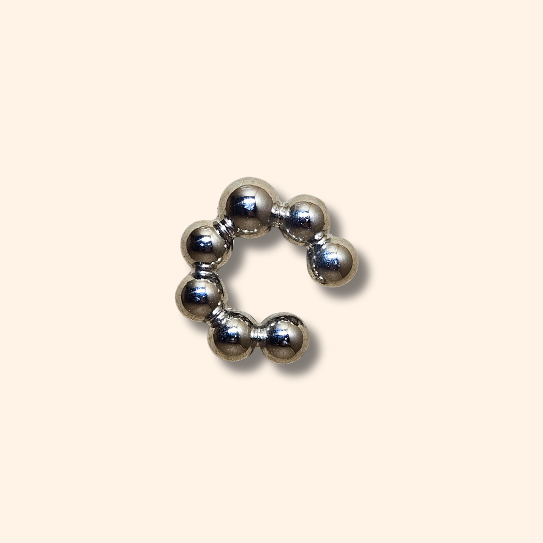 The Seven Spheres Ear Cuff by Roots Jewellery, crafted from stainless steel, is a fashionable accessory adorned with gold beads elegantly set against a beige background.