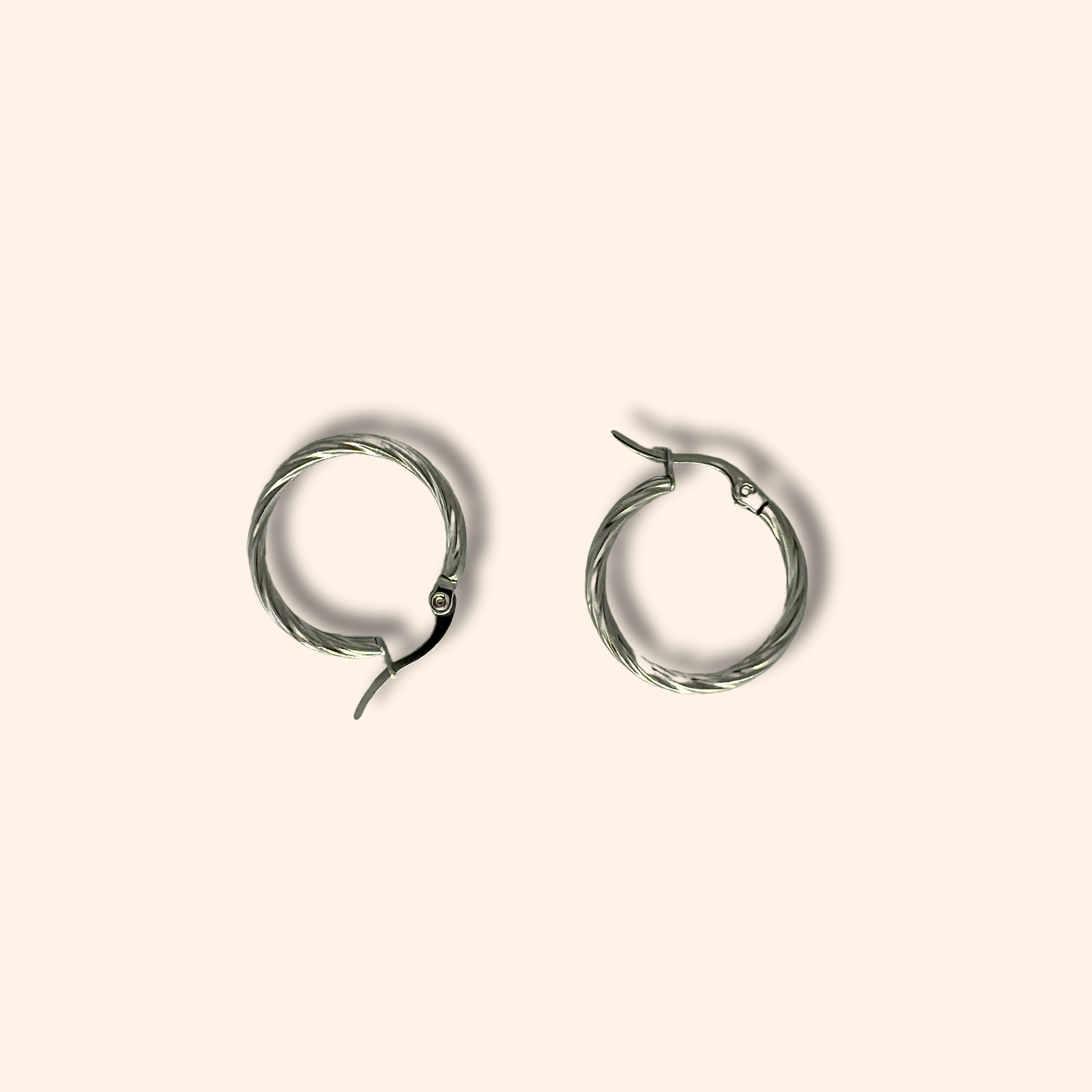 Two timeless Silver Small Spiral Hoop Earrings by Roots Jewellery, showcasing a twisted design, set against a light beige background.