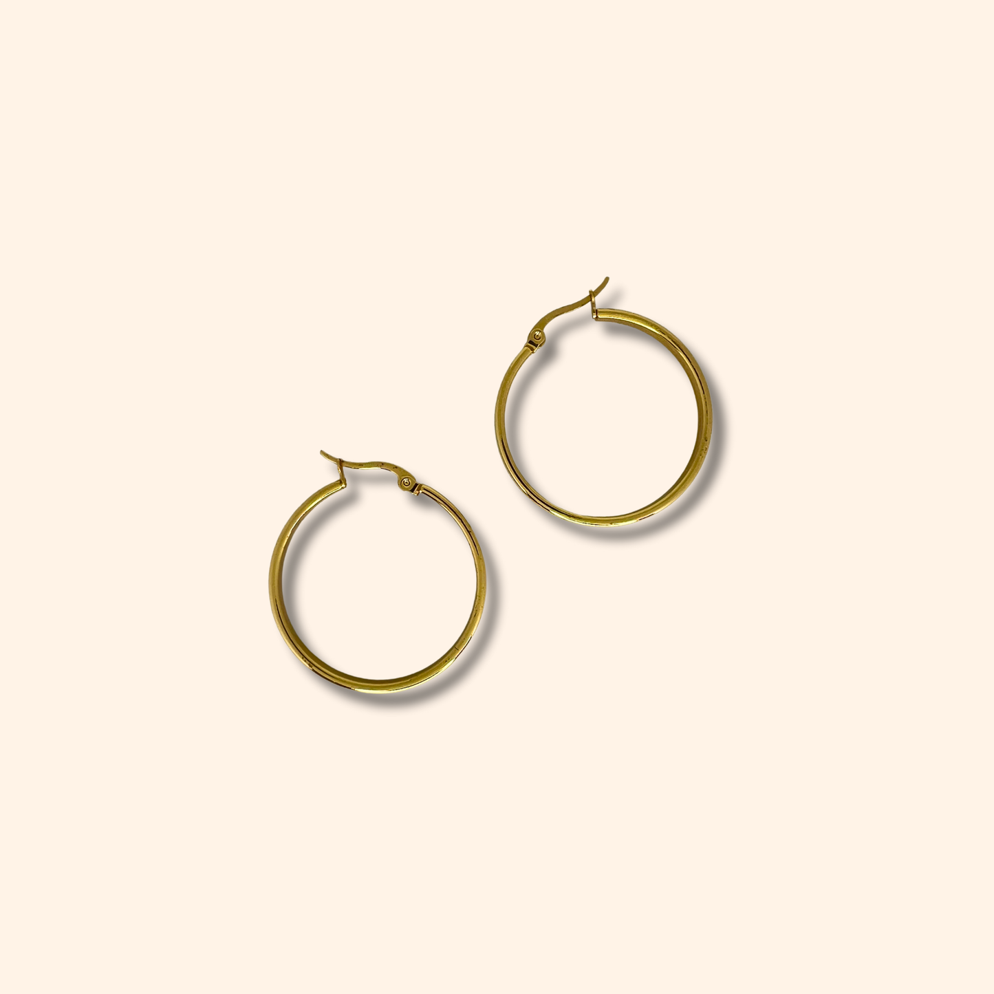 Discover the Gold Smooth Hoop Earrings from Roots Jewellery, set against a light beige backdrop. Meticulously crafted, these earrings boast a timeless elegance that effortlessly surpasses fleeting trends, establishing them as an essential piece in any jewelry collection.