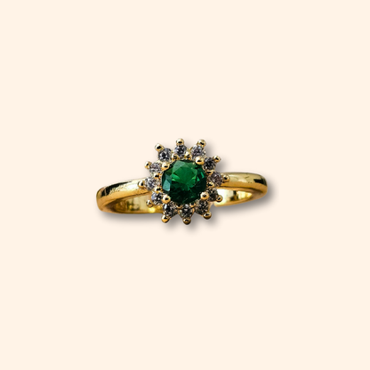 The Emerald Flower Gold Ring by Roots Jewellery features a stunning green emerald at its center, accented by dazzling clear stones. Its sophisticated design is set on a simple backdrop and includes an adjustable feature for the ideal fit.