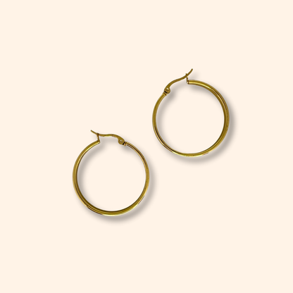 Discover the Gold Smooth Hoop Earrings from Roots Jewellery, set against a light beige backdrop. Meticulously crafted, these earrings boast a timeless elegance that effortlessly surpasses fleeting trends, establishing them as an essential piece in any jewelry collection.