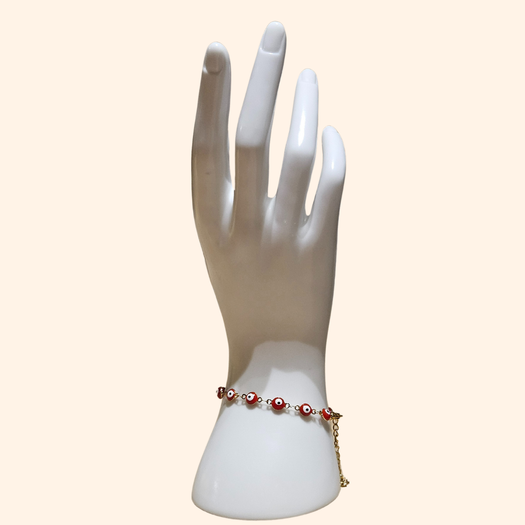 A mannequin hand elegantly showcases the Evil Eye Bracelet - Single Colour by Roots Jewellery, featuring handcrafted red and white beads on a gold chain, merging style with protection.