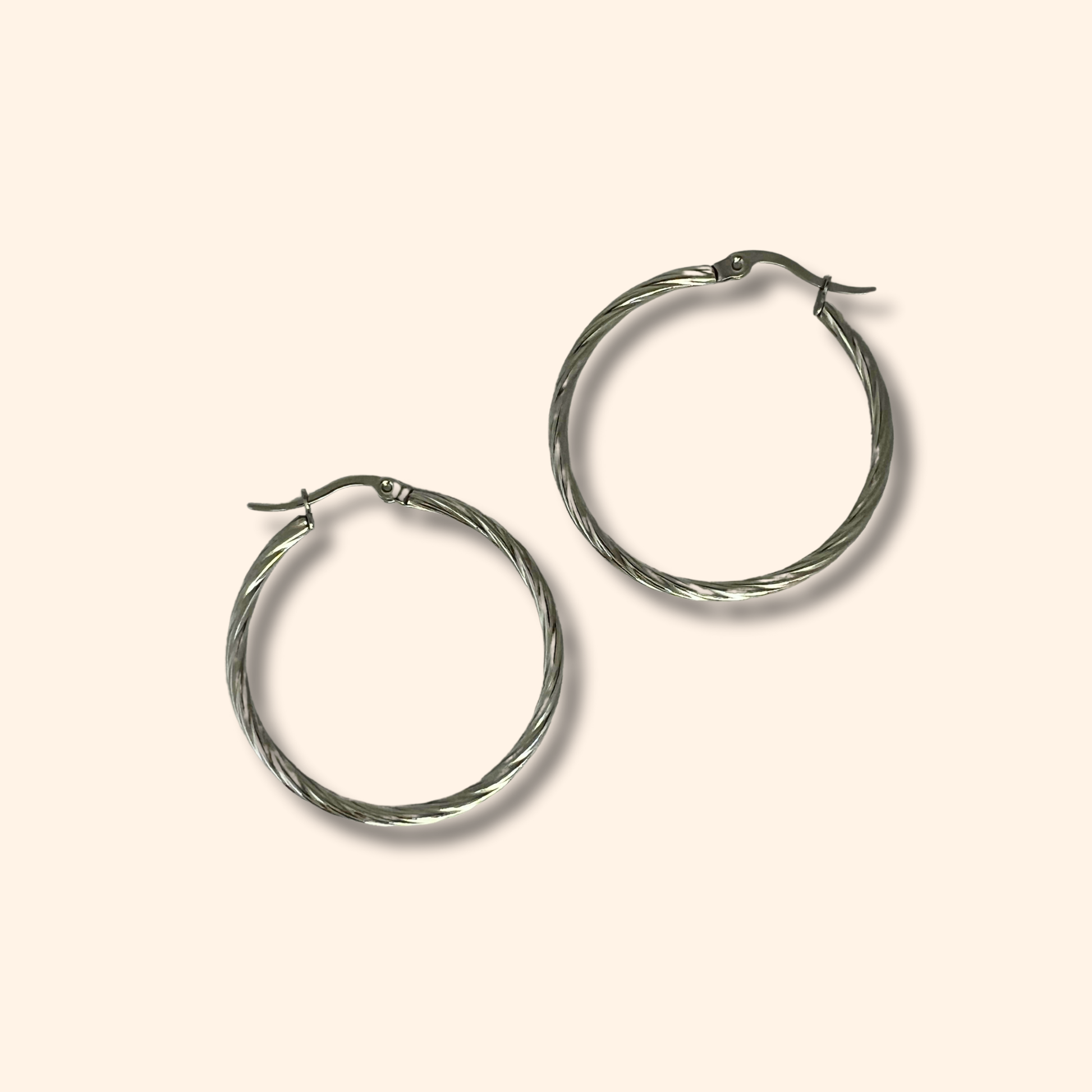 Two Roots Jewellery Silver Medium Spiral Hoop Earrings, made from stainless steel featuring a twisted design, are elegantly showcased on a neutral background.