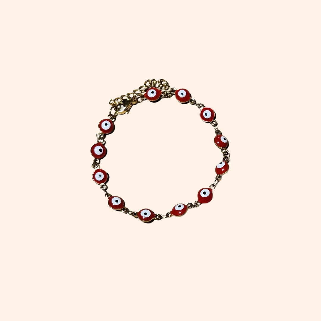 A mannequin hand elegantly showcases the Evil Eye Bracelet - Single Colour by Roots Jewellery, featuring handcrafted red and white beads on a gold chain, merging style with protection.