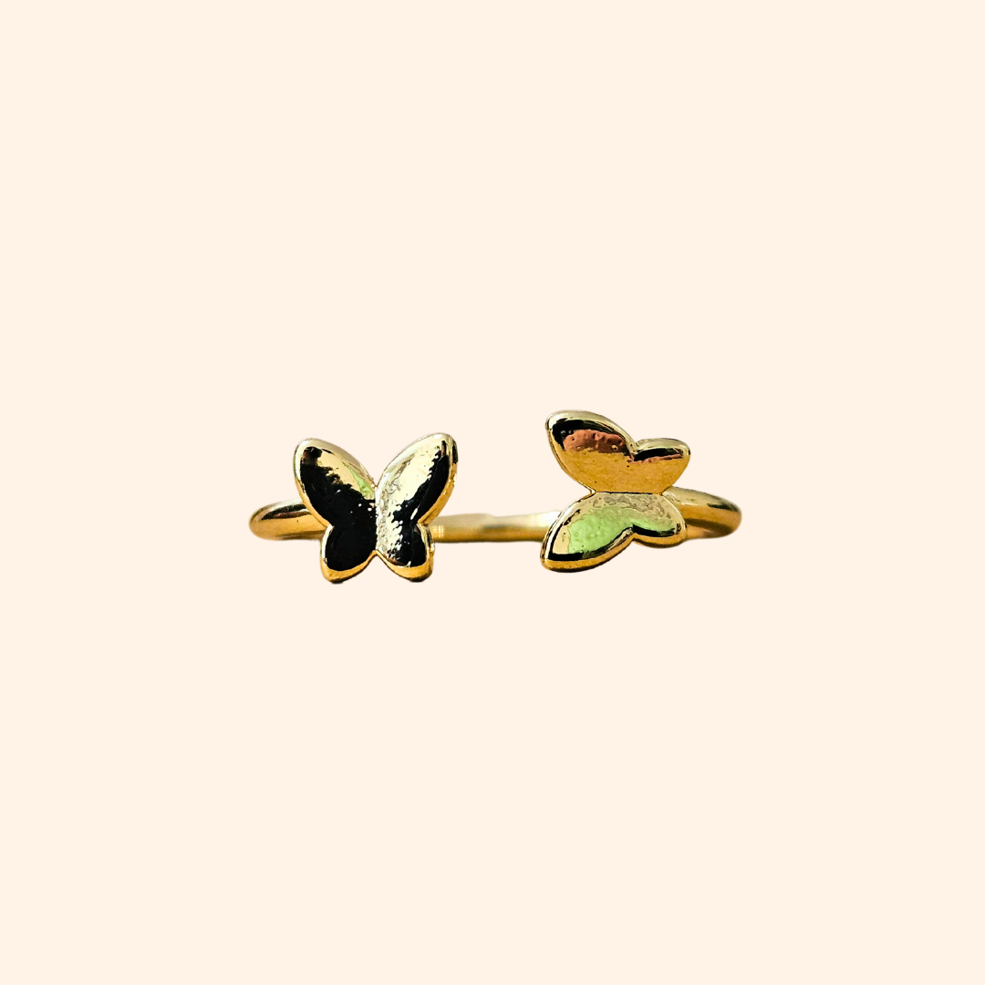 Embrace sophistication with the Butterfly Gold Ring from Roots Jewellery. This adjustable ring showcases two butterfly-shaped accents in black and green enamel against a beige background, providing both style and comfort. It's an exquisite addition to any jewelry collection.