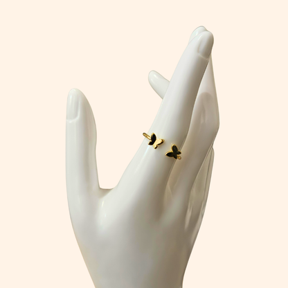 Embrace sophistication with the Butterfly Gold Ring from Roots Jewellery. This adjustable ring showcases two butterfly-shaped accents in black and green enamel against a beige background, providing both style and comfort. It's an exquisite addition to any jewelry collection.