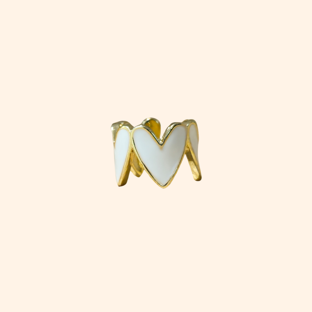 This chic accessory is the Heart-shaped Ear Cuff by Roots Jewellery, showcasing a gold finish with a repeating white heart pattern on a light beige background.