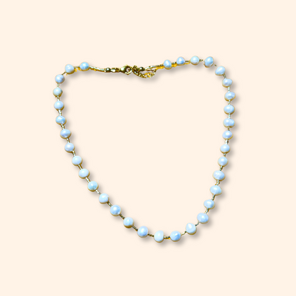 The Pearl Necklace by Roots Jewellery, featuring a gold clasp and freshwater pearls, exudes grace and sophistication as it rests elegantly on a light beige background.