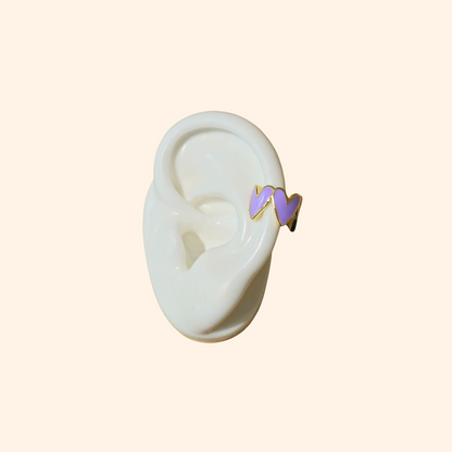 This chic accessory is the Heart-shaped Ear Cuff by Roots Jewellery, showcasing a gold finish with a repeating white heart pattern on a light beige background.