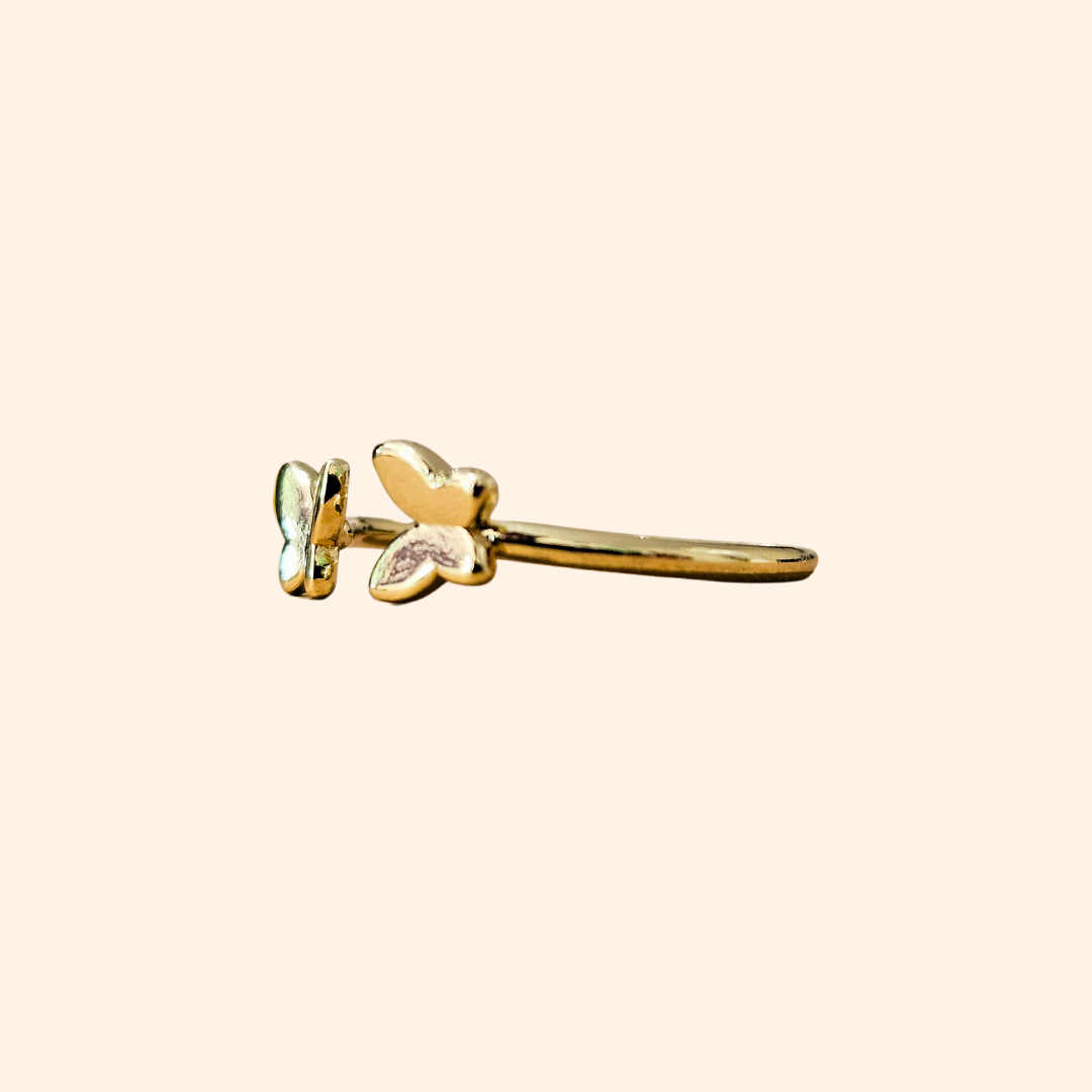 Embrace sophistication with the Butterfly Gold Ring from Roots Jewellery. This adjustable ring showcases two butterfly-shaped accents in black and green enamel against a beige background, providing both style and comfort. It's an exquisite addition to any jewelry collection.