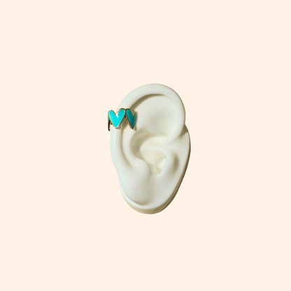 This chic accessory is the Heart-shaped Ear Cuff by Roots Jewellery, showcasing a gold finish with a repeating white heart pattern on a light beige background.