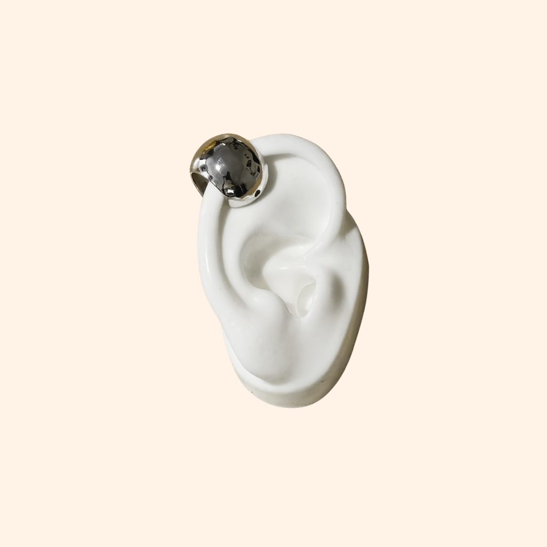 The Dome Shape Ear Cuff by Roots Jewellery features a shiny, metallic open-ended design, elegantly highlighting its dome style against a plain backdrop. This versatile accessory is perfect for adding an edgy touch to any style, resembling a sleek stainless steel ear cuff.