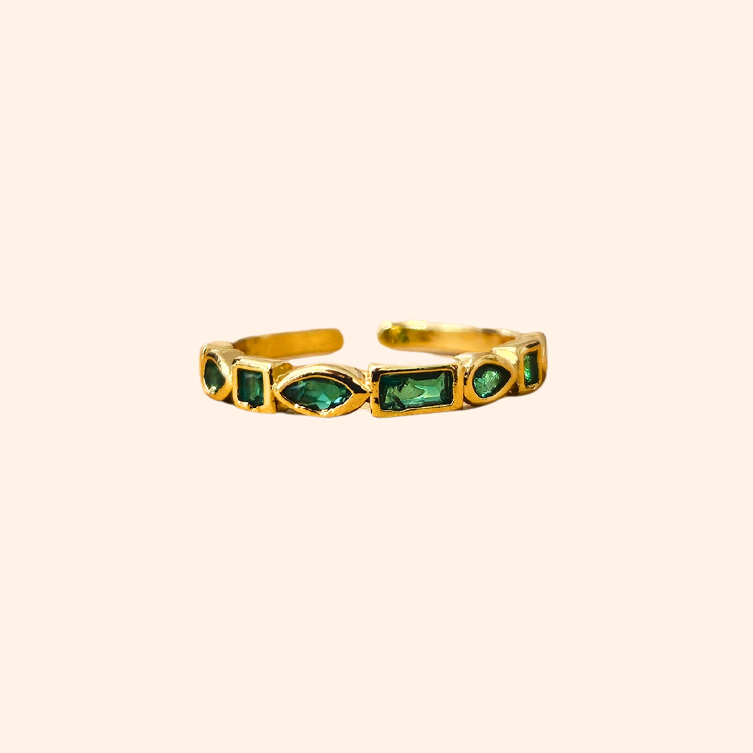 Eternity Green Gold Ring by Roots Jewellery featuring vibrant emerald zircons set in a continuous pattern on a plain beige background.