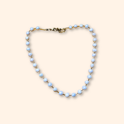 The Pearl Necklace by Roots Jewellery, featuring a gold clasp and freshwater pearls, exudes grace and sophistication as it rests elegantly on a light beige background.