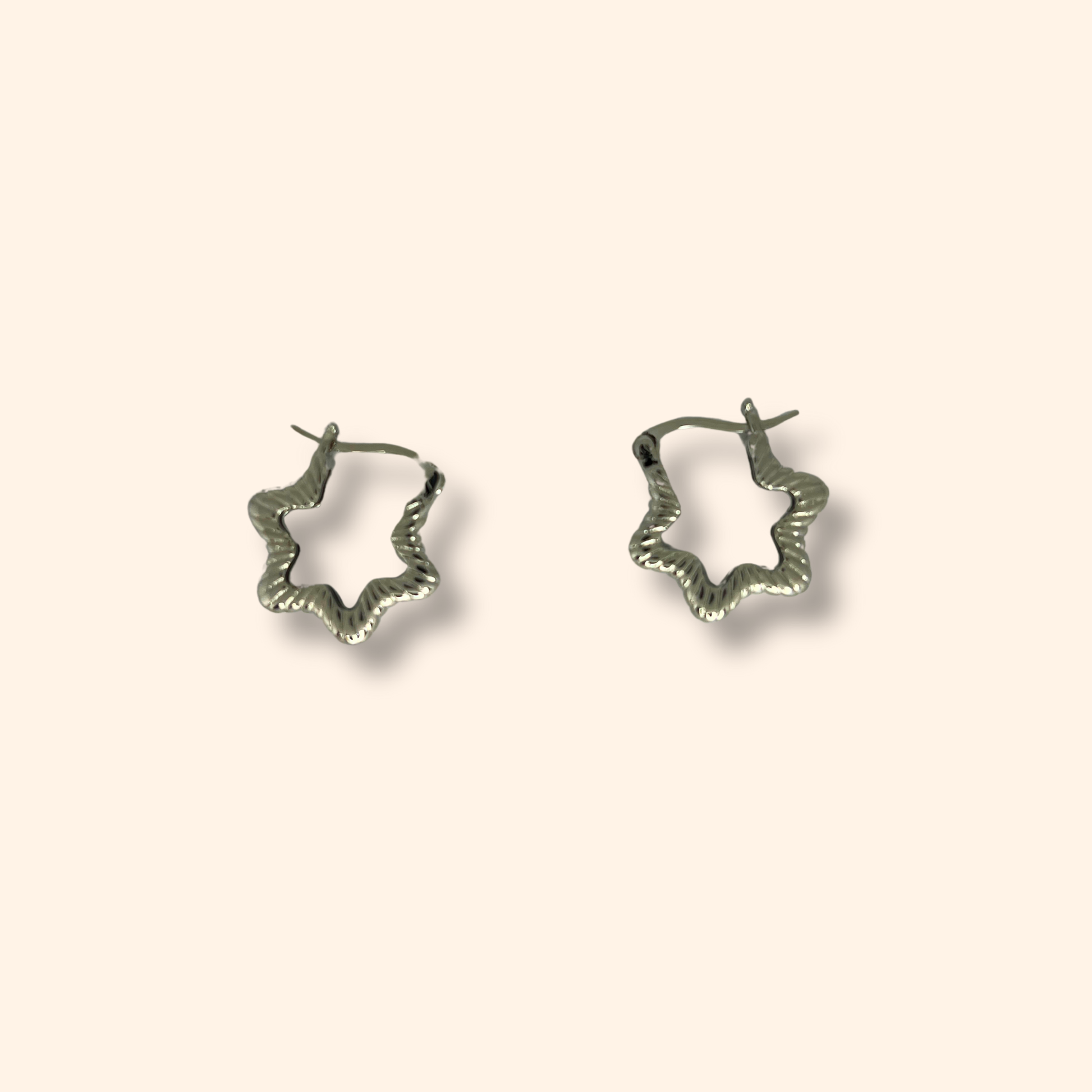 Experience the elegance of Roots Jewellery's Silver Star Hoop Earrings, rhodium-plated and showcasing a captivating star design that stands out beautifully against a simple beige backdrop.