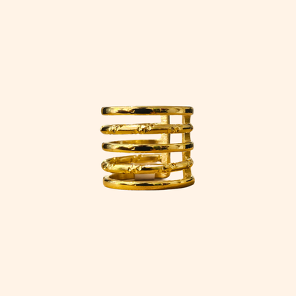 The Infinite Hoops Gold Ring from Roots Jewellery beautifully features several slender bands stacked vertically, forming an opulent spiral design against a beige backdrop.