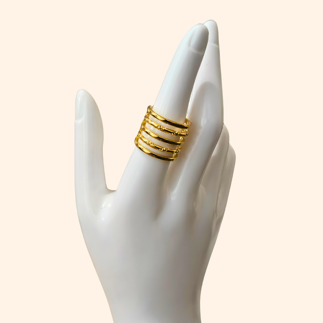 The Infinite Hoops Gold Ring from Roots Jewellery beautifully features several slender bands stacked vertically, forming an opulent spiral design against a beige backdrop.