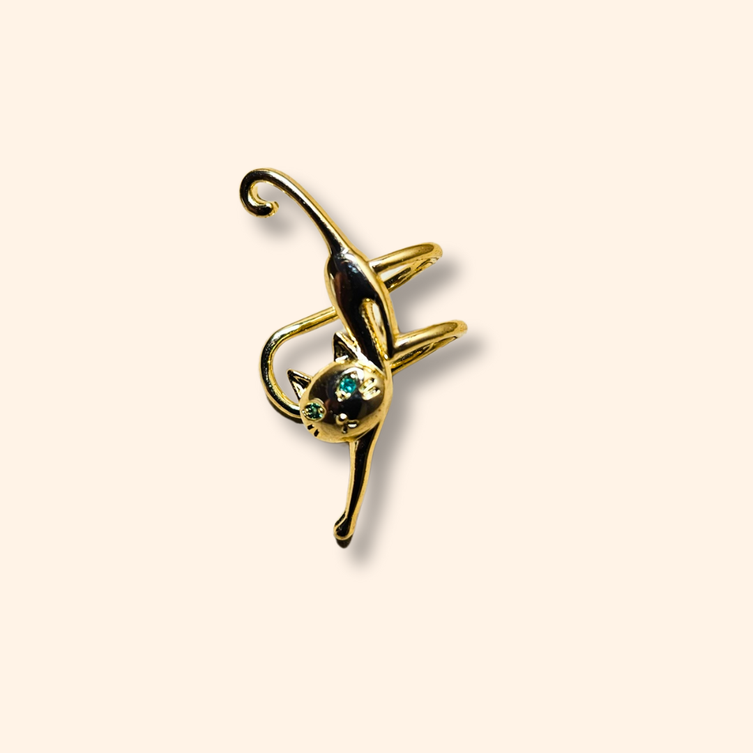 The Cat Climber gold ear cuff by Roots Jewellery is designed in the shape of a stretching cat, with two captivating green gemstones for eyes, set on a sleek background. This unique and elegant accessory effortlessly enhances your look.