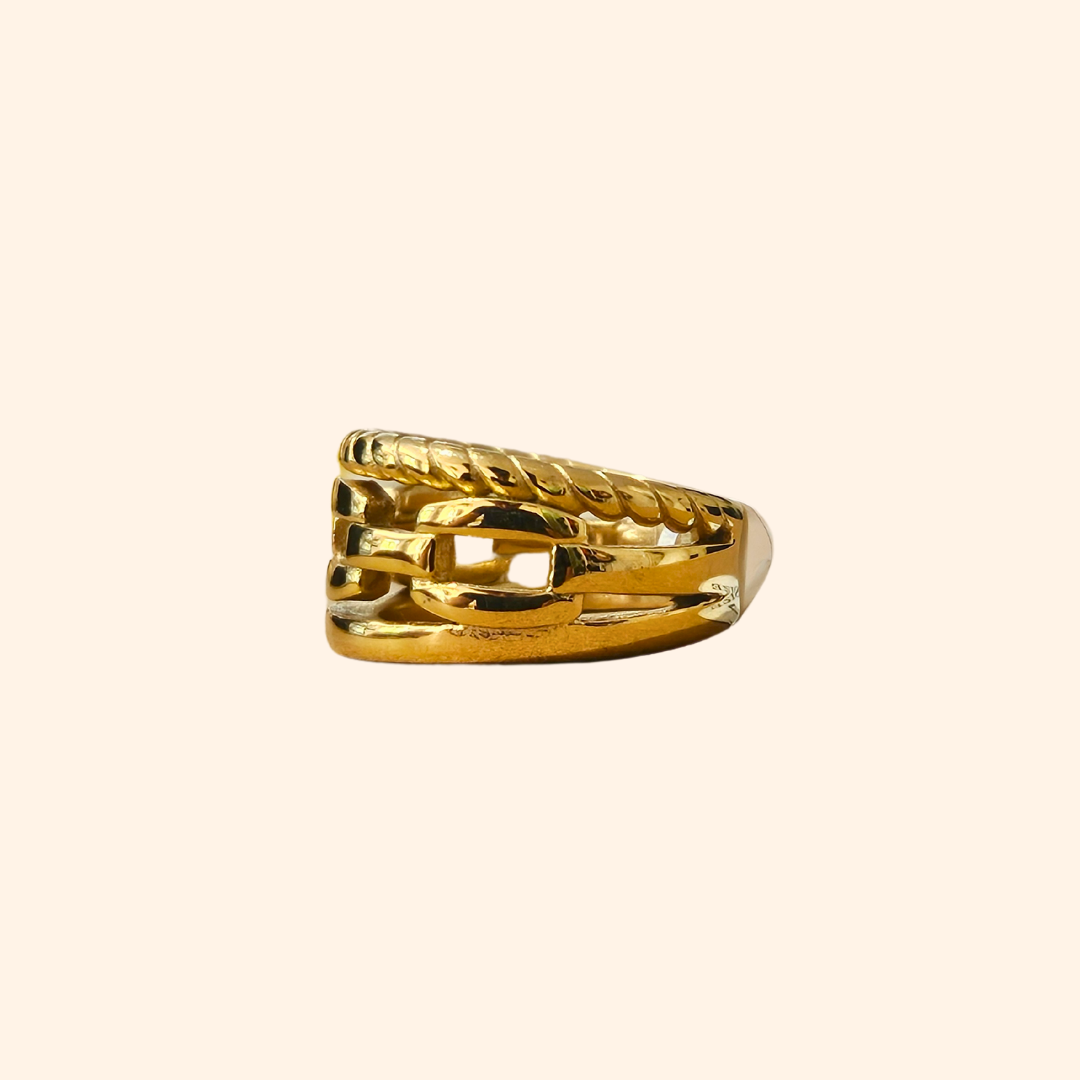 A Chain Gold Ring by Roots Jewellery, featuring a timeless interwoven design, graces a beige background.