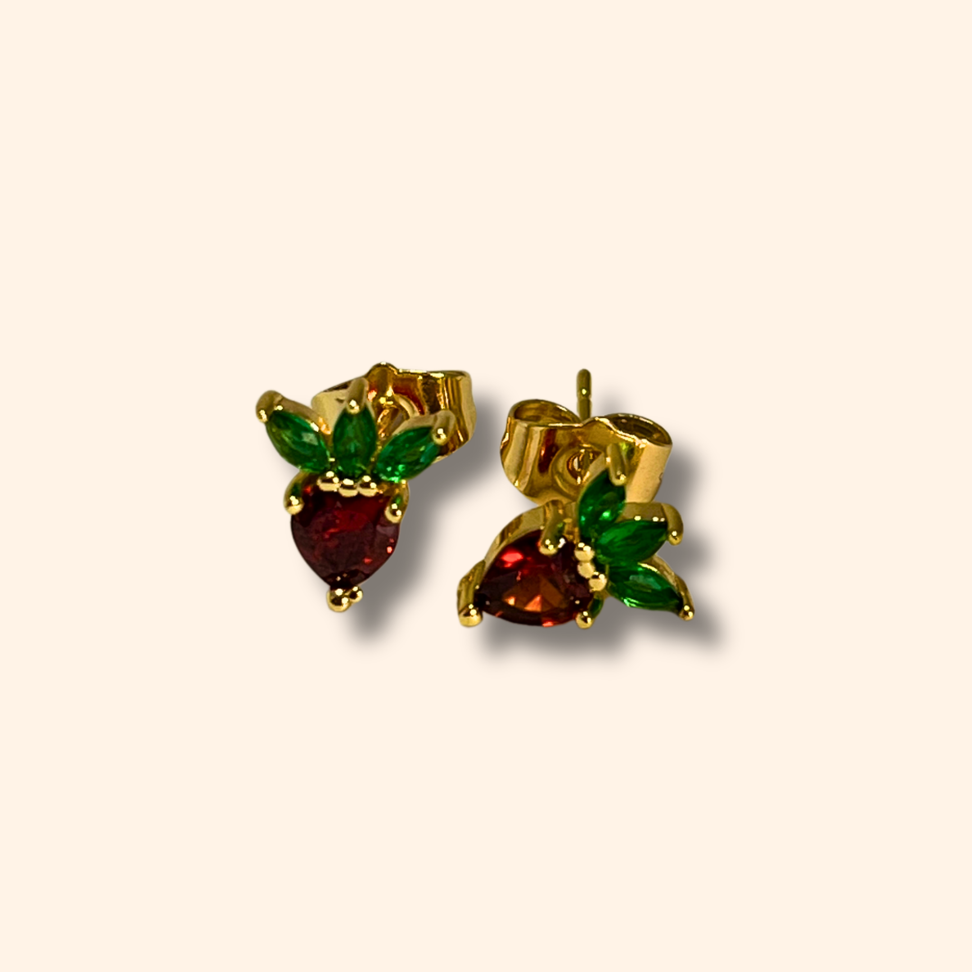 Introducing the Zirconia Strawberries Gold Earrings from Roots Jewellery: these elegant earrings boast red zirconia gemstone centers and green leaf-shaped accents, all set in a classic gold stud design. Perfect for infusing any outfit with a hint of luxury.