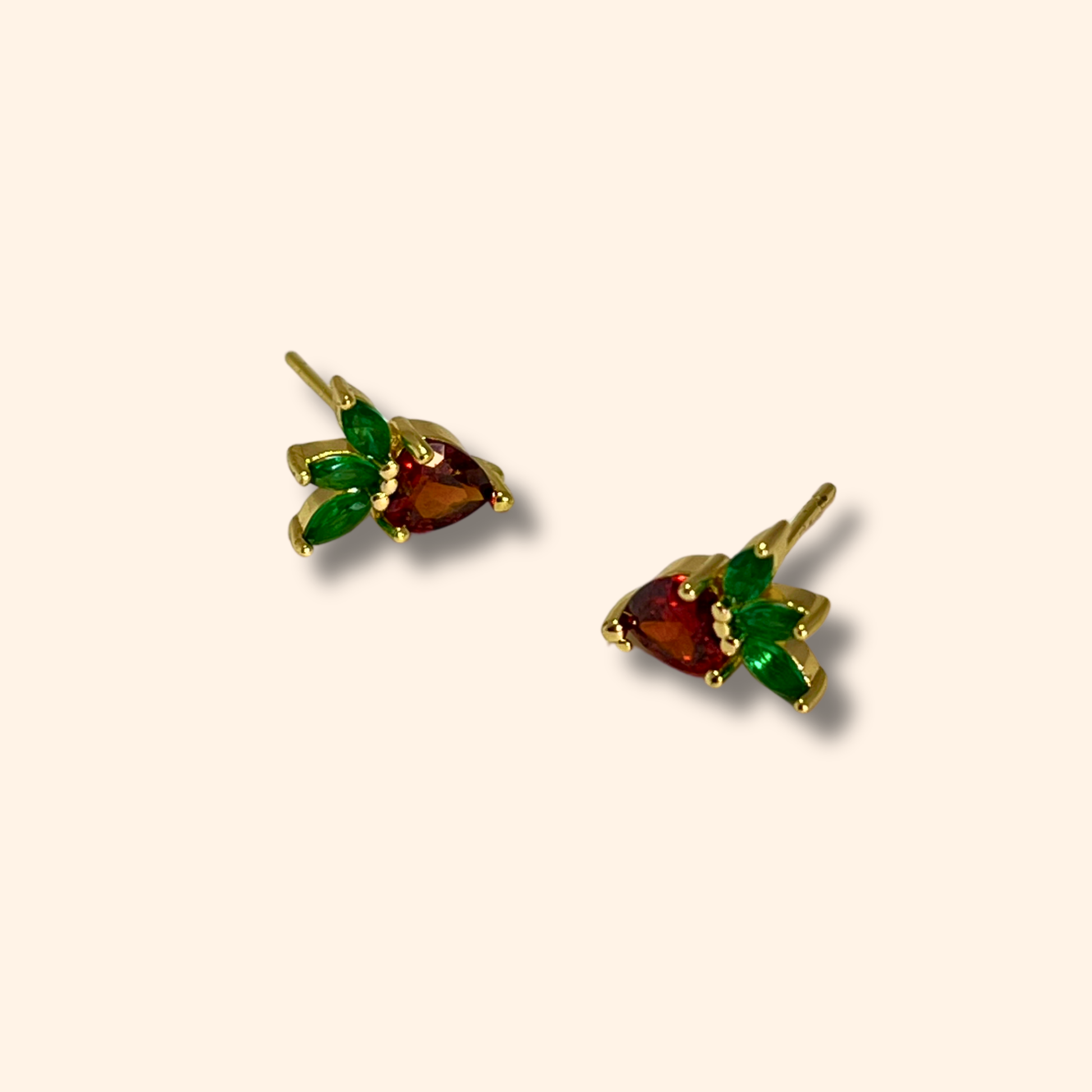 Introducing the Zirconia Strawberries Gold Earrings from Roots Jewellery: these elegant earrings boast red zirconia gemstone centers and green leaf-shaped accents, all set in a classic gold stud design. Perfect for infusing any outfit with a hint of luxury.