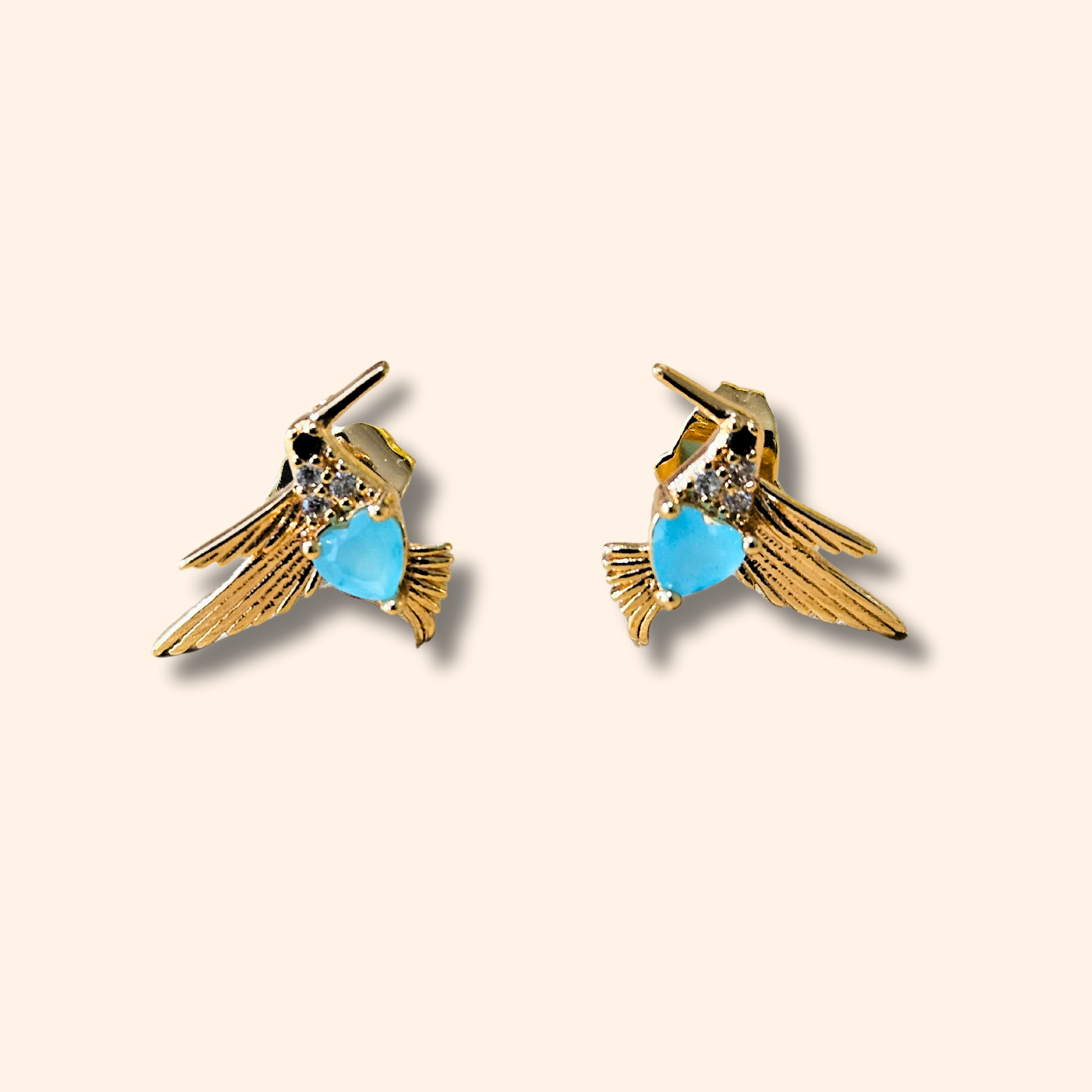 Roots Jewellery's Gold and Blue Bird Earrings grace a beige backdrop, ideal for those who appreciate nature-inspired elegance with a hint of animal charm.