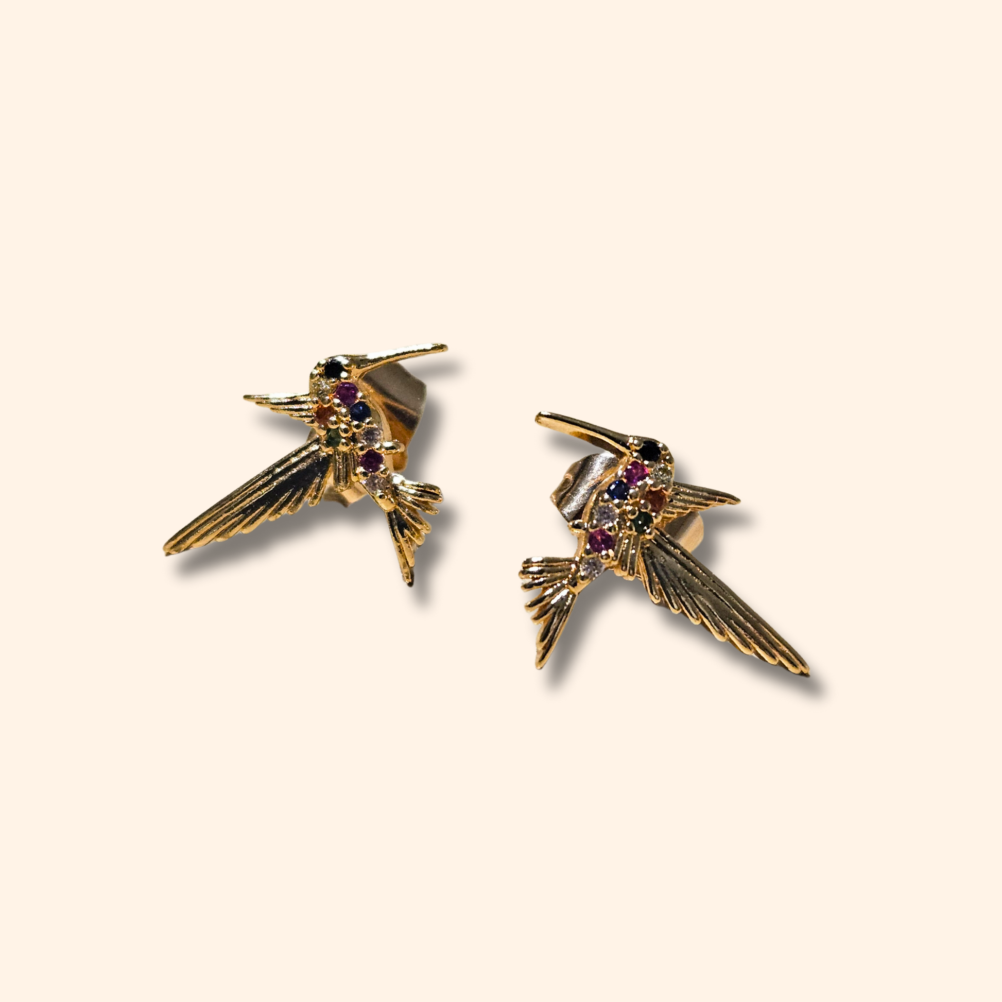 A pair of Rainbow Gold Hummingbird Earrings by Roots Jewellery, adorned with purple gem accents on a white backdrop and crafted with vibrant multicolour zircons for an extra touch of sparkle.