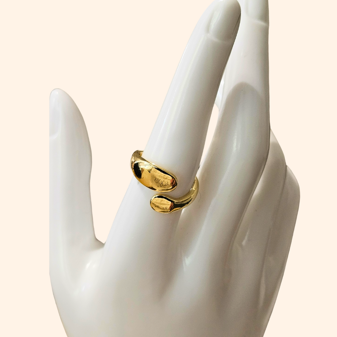 Discover the Double Twist Gold Ring by Roots Jewellery, showcasing a gold open-ended design with smooth, curved elegance on a light background. This exquisite piece ensures a perfect fit every time with its adjustable sizing feature.