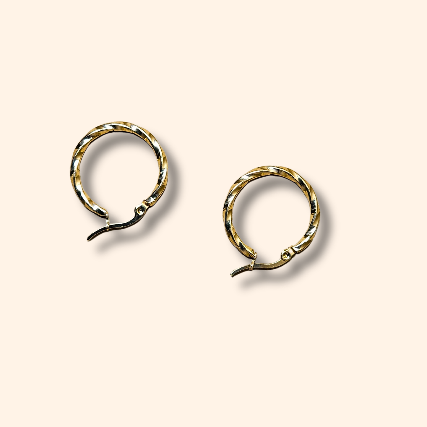 Two Gold Small Spiral Hoop Earrings by Roots Jewellery, featuring versatile clasp closures, rest elegantly on a light beige background.