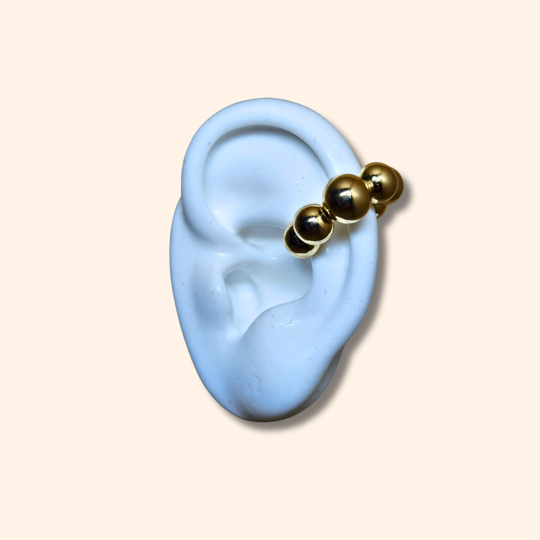 The Seven Spheres Ear Cuff by Roots Jewellery, crafted from stainless steel, is a fashionable accessory adorned with gold beads elegantly set against a beige background.