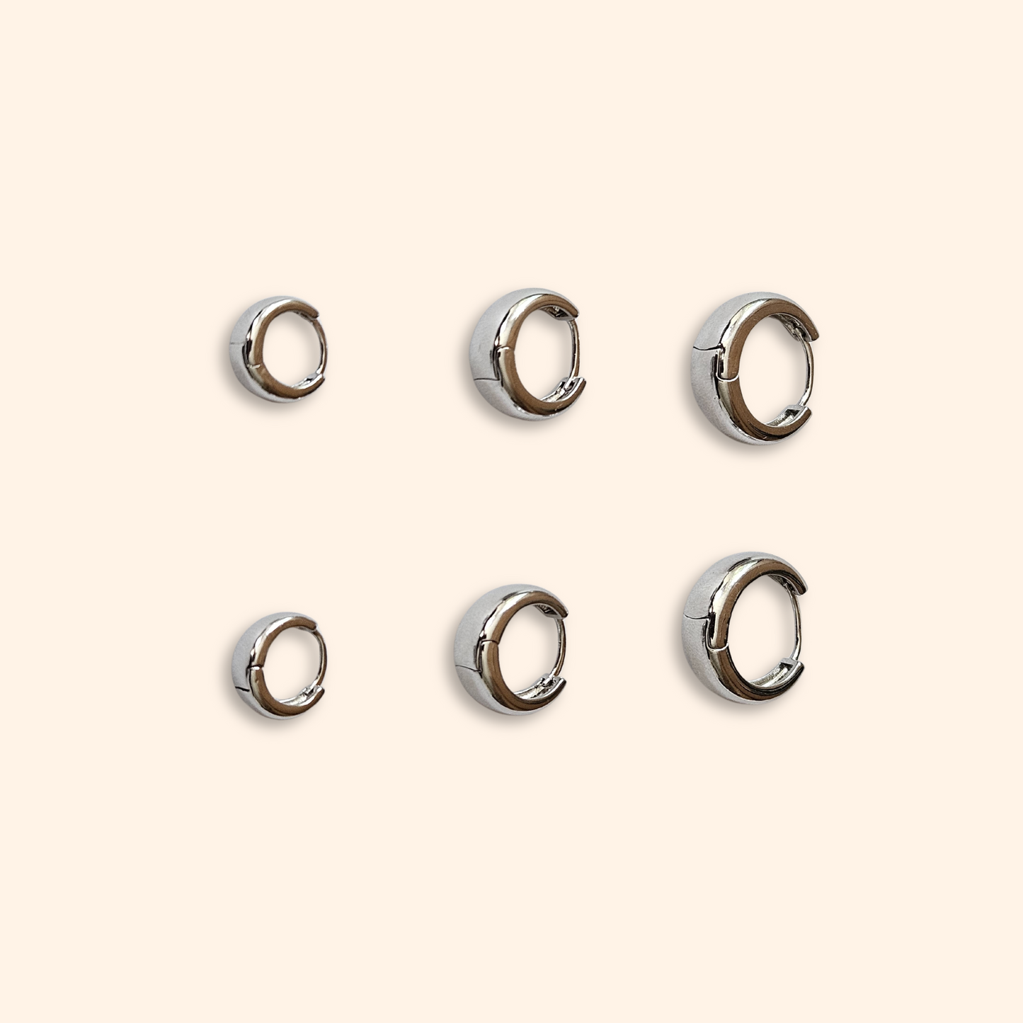 Five pairs of exquisite hoop earrings from the Roots Jewellery's "3 Set Hoop Earrings" collection gleam on a light beige background, showcasing their stunning elegance. Available in both gold and silver finishes, these elegant pieces are perfect for any occasion.