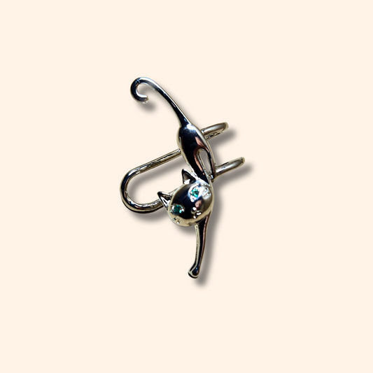 Introducing the Cat Climber - Silver - Ear Cuff by Roots Jewellery, a chic accessory showcasing a cat-shaped pin with captivating blue eyes set against a beige backdrop, expertly crafted using durable stainless steel.