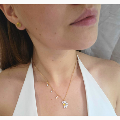 A woman is elegantly dressed in a white top, accessorized with a stainless steel daisy-shaped earring and the Daisy Necklace from Roots Jewellery.