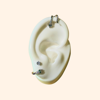 A mannequin ear displays the Sparkling Ivy Trio Earrings from Roots Jewellery, highlighting a vine-like design with a dangling earring at the top, a stud on the lobe, and a hoop adorned with zircon stones near the bottom.