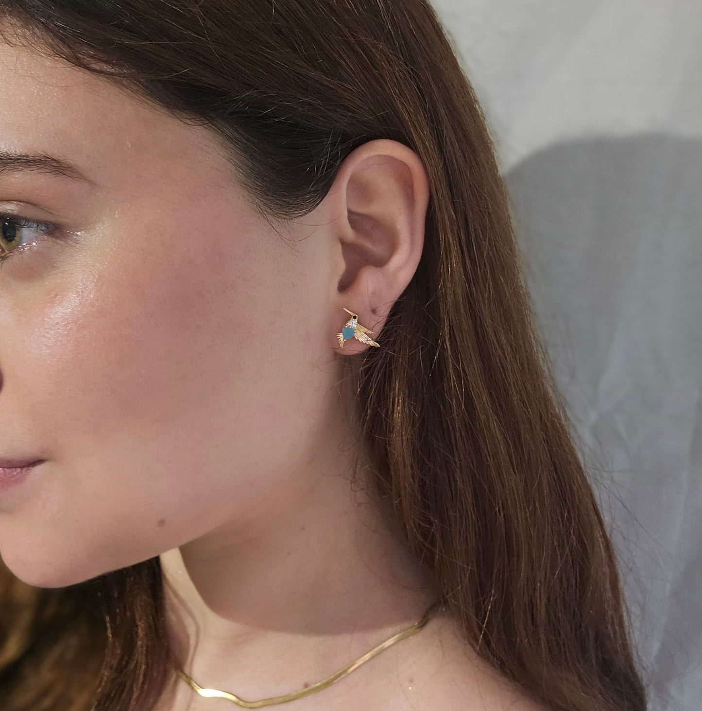 Roots Jewellery's Gold and Blue Bird Earrings grace a beige backdrop, ideal for those who appreciate nature-inspired elegance with a hint of animal charm.