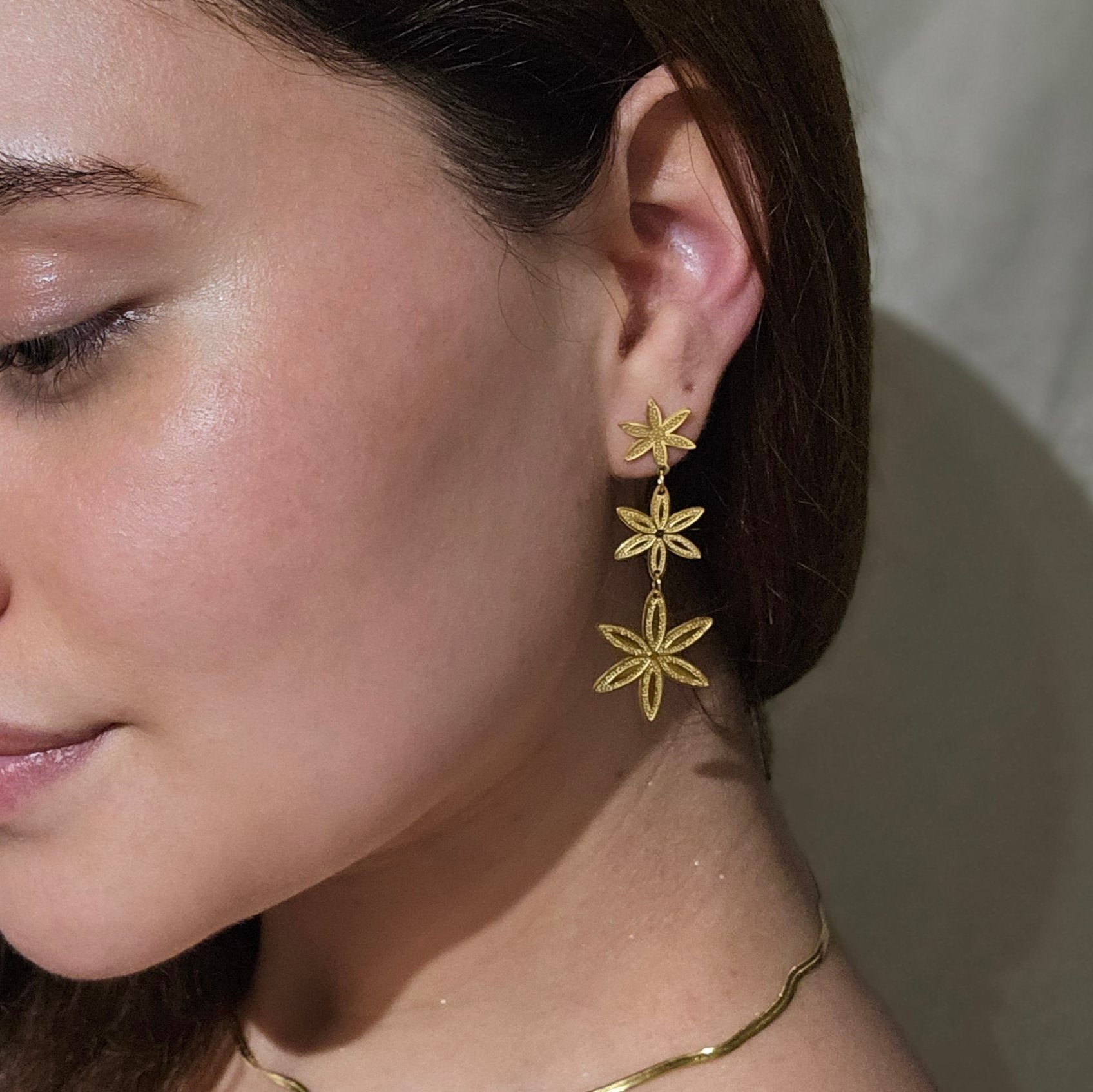 Close-up of a person elegantly adorned in golden flowers, featuring the Golden Flower Rain Earrings by Roots Jewellery and a matching gold necklace.