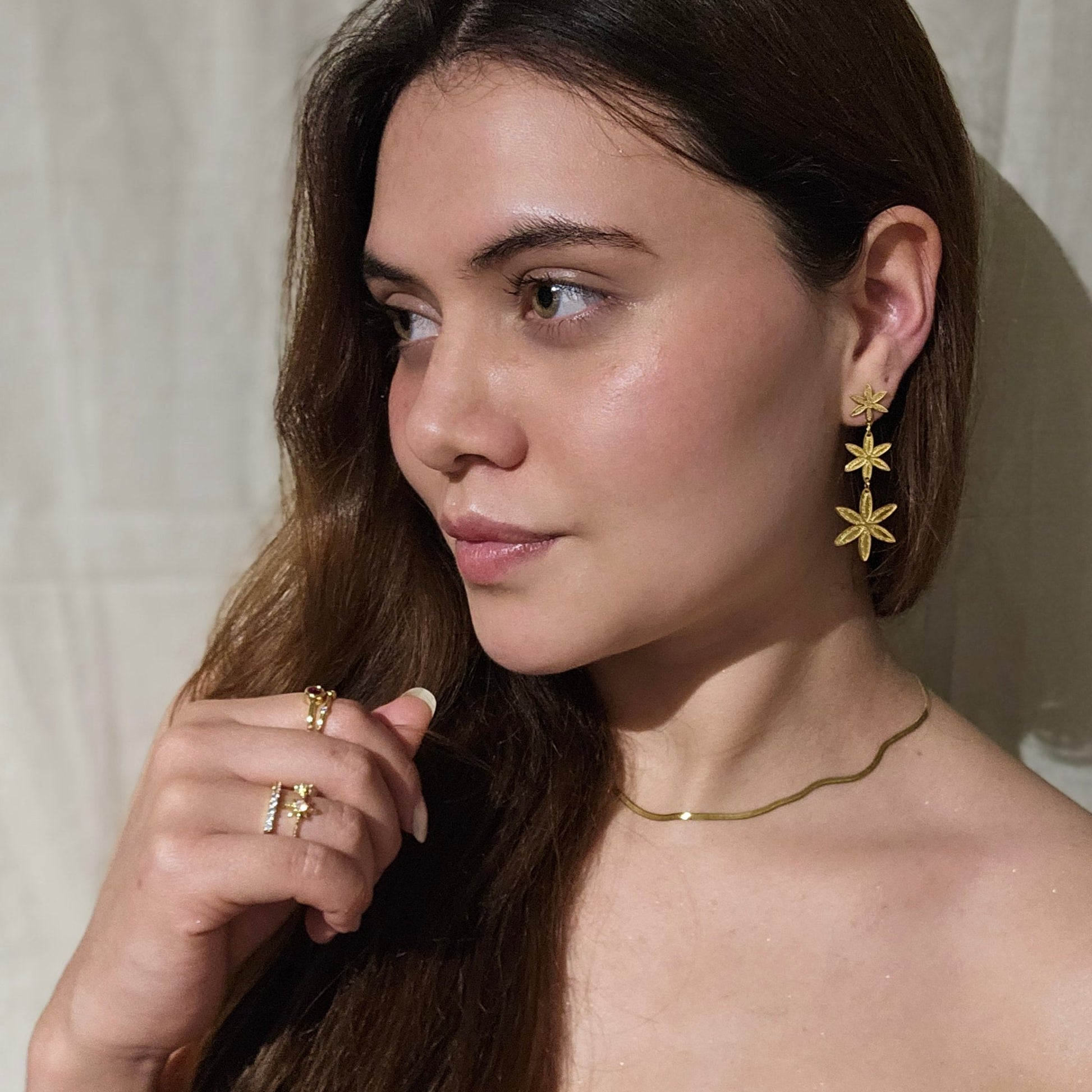 Close-up of a person elegantly adorned in golden flowers, featuring the Golden Flower Rain Earrings by Roots Jewellery and a matching gold necklace.