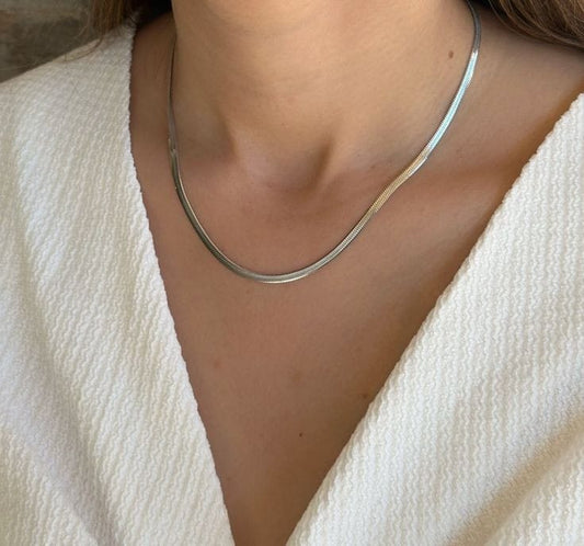 A person is adorned in a white textured outfit complemented by a classic piece from Roots Jewellery: the Silver Snake Chain Necklace, celebrated for its elegant design.