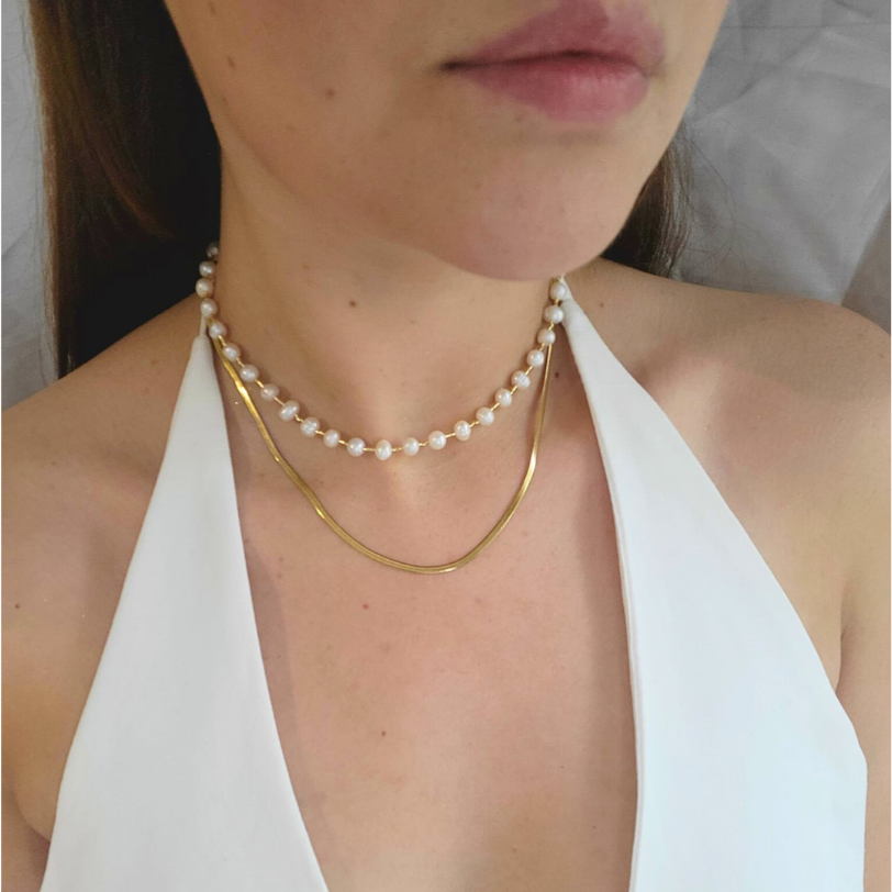 The Pearl Necklace by Roots Jewellery, featuring a gold clasp and freshwater pearls, exudes grace and sophistication as it rests elegantly on a light beige background.