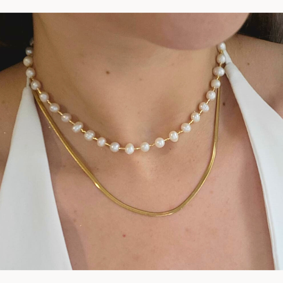 The Pearl Necklace by Roots Jewellery, featuring a gold clasp and freshwater pearls, exudes grace and sophistication as it rests elegantly on a light beige background.