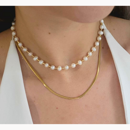 The Pearl Necklace by Roots Jewellery, featuring a gold clasp and freshwater pearls, exudes grace and sophistication as it rests elegantly on a light beige background.