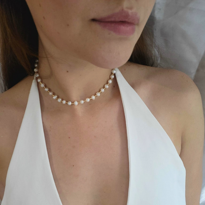 The Pearl Necklace by Roots Jewellery, featuring a gold clasp and freshwater pearls, exudes grace and sophistication as it rests elegantly on a light beige background.