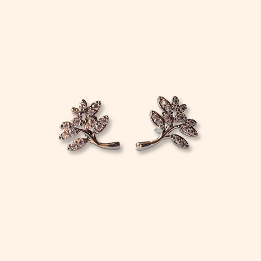 Tree-shaped earrings from Roots Jewellery, adorned with small crystals, beautifully capture the essence of nature when set against a beige background.