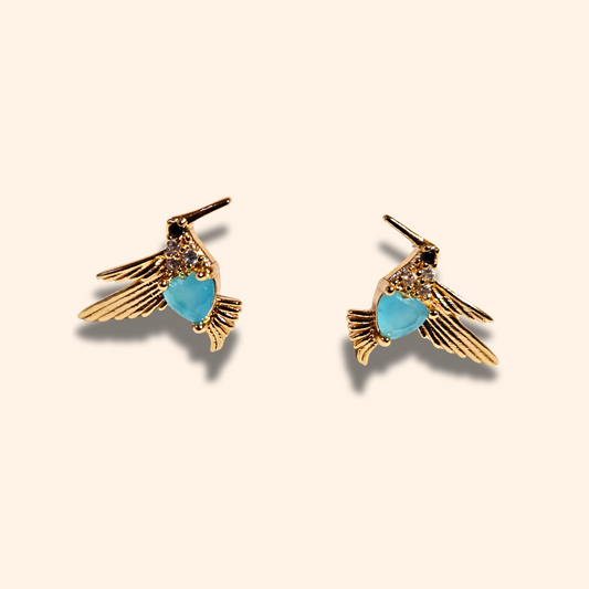 Roots Jewellery's Gold and Blue Bird Earrings grace a beige backdrop, ideal for those who appreciate nature-inspired elegance with a hint of animal charm.