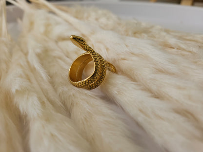 A hand adorned with a Golden Snake Ring by Roots Jewellery and black-tipped nails rests gracefully on soft, white pampas grass.