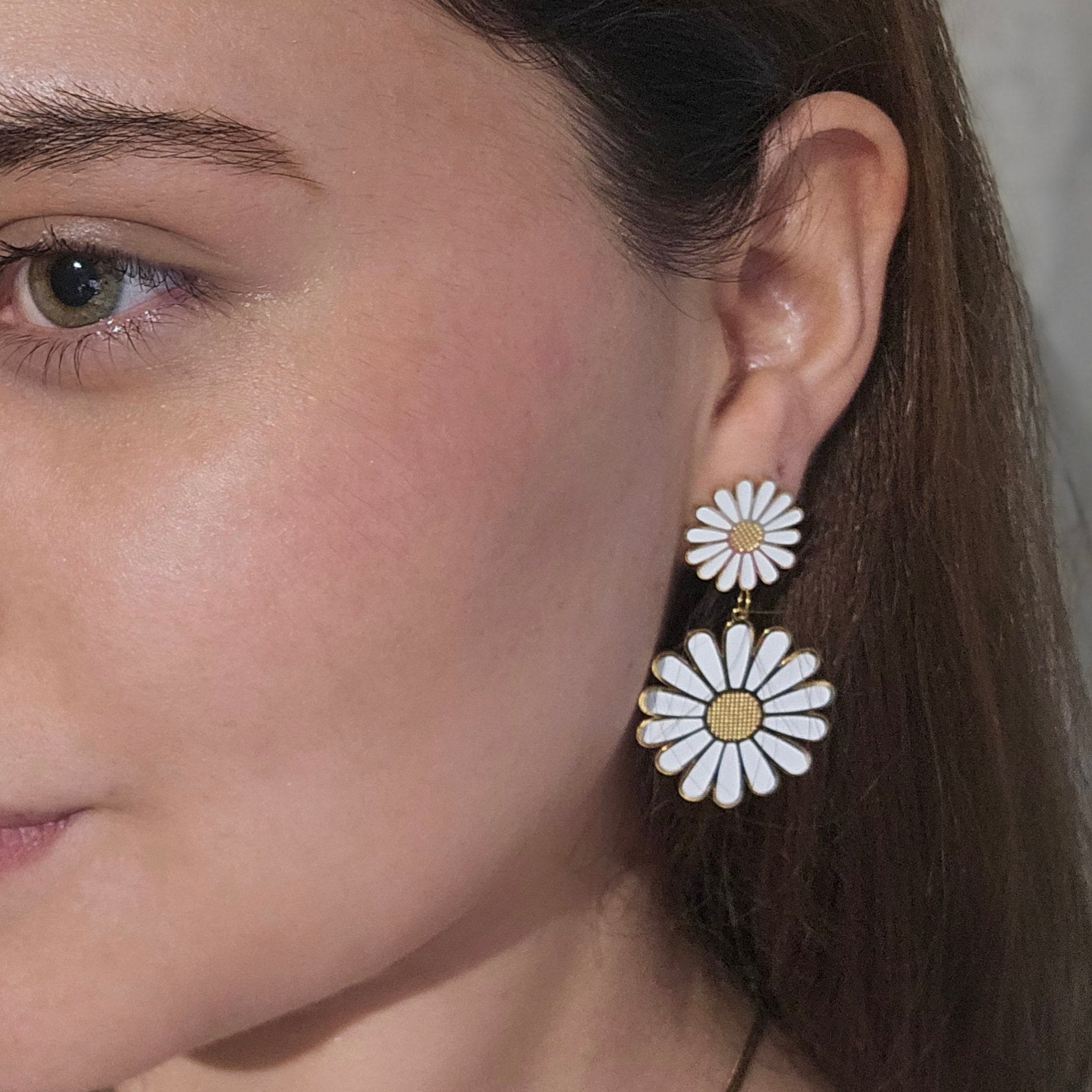 Close-up of a person wearing Roots Jewellery's White Daisy Bloom Earrings, an elegantly crafted statement piece in stainless steel. The neutral background enhances the design as the person is slightly turned to the side, allowing the earrings to effortlessly stand out.