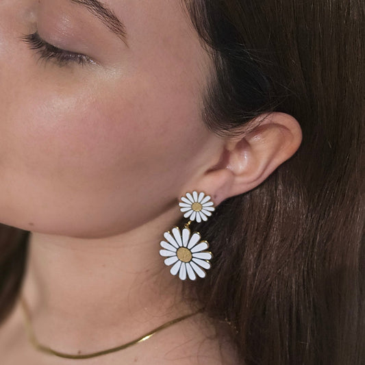 Close-up of a person wearing Roots Jewellery's White Daisy Bloom Earrings, an elegantly crafted statement piece in stainless steel. The neutral background enhances the design as the person is slightly turned to the side, allowing the earrings to effortlessly stand out.